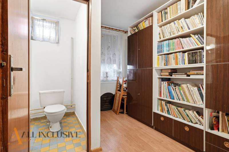 Na predaj 4-izb. rodinný dom s garážou, Okoč - Toaleta s dlažbou vedľa izby s knihovnicou a podlahou s dreveným dekorom v rodinnom dome.