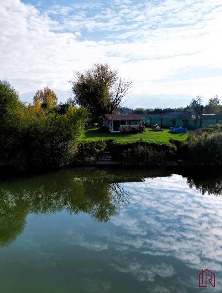 KH-1018, PREDAJ Pozemok pri jazere 887 m², garáž, altánok - Výstavba domov v Čani, pri vode s chatkou na tráve a stromami.