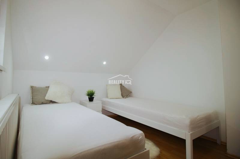 EXKLUZÍVNE / RODINNÝ DOM NA PREDAJ V OBCI SÚĽOV - Spálňa v rodinnom dome s dvomi posteľami a stolíkom, podlaha s dreveným dekorom.