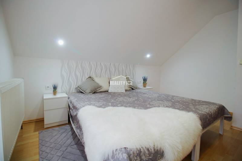 EXKLUZÍVNE / RODINNÝ DOM NA PREDAJ V OBCI SÚĽOV - Spálňa v rodinnom dome s posteľou, vankúšmi a nočnými stolíkmi na podlahe s dreveným dekorom.