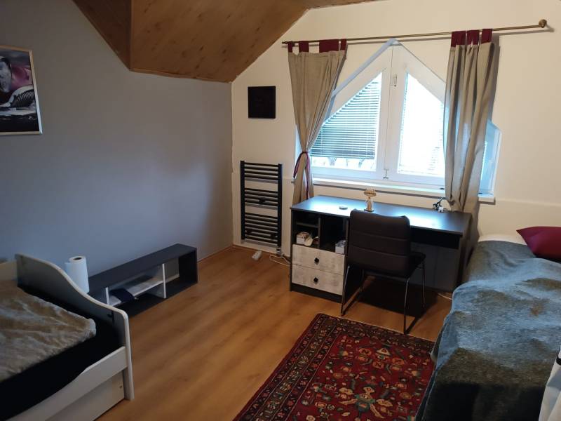 Na predaj rodinný dom Orovnica - Izba v rodinnom dome s podlahou s dreveným dekorom, písací stôl, posteľ a koberec.