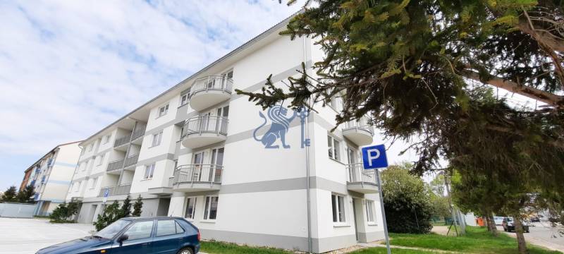 Na predaj 2 izb. byt s balkónom blízko centra, Chorvátsky Grob - Budova na Školskej ulici v Chorvátskom Grobe so zaparkovaným autom v pozadí.