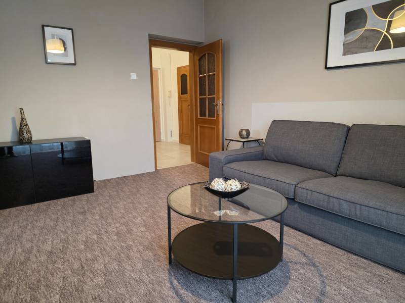 PRENÁJOM - Priestranný 3 izbový byt - Nitra, Centrum - Obývacia izba v 3-izbovom byte so sivou sedačkou a preskleným stolom.