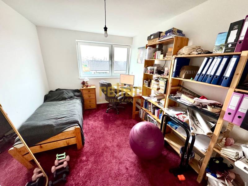 Moderný radový rodinný dom v Novej Dedinke, projekt “Lastovičky” - Izba v rodinnom dome so stolom, posteľou, policami a červeným kobercom.