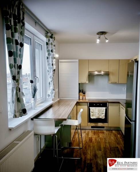 Prenájom moderný a svetlý 3-izbový byt v atraktívnej lokalite - Kuchyňa v 3-izbovom byte s barovým pultom, podlahou s dreveným dekorom a veľkým oknom.