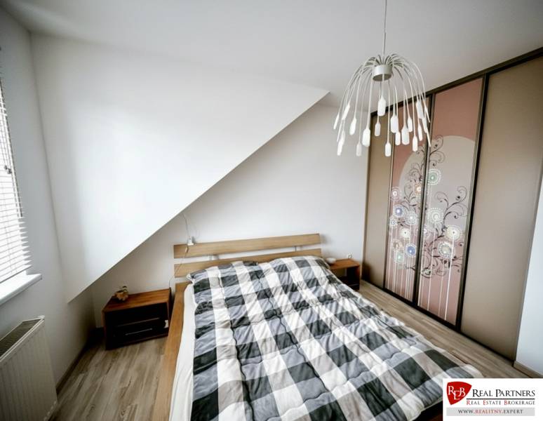 Prenájom moderný a svetlý 3-izbový byt v atraktívnej lokalite - Spálňa v 3-izbovom byte s posteľou, vstavanou skriňou a podlahou s dreveným dekorom.