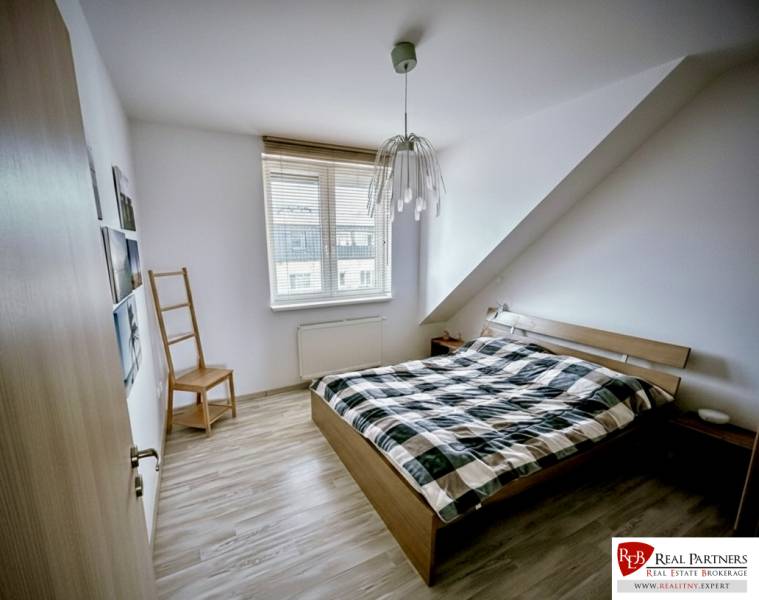 Prenájom moderný a svetlý 3-izbový byt v atraktívnej lokalite - Spálňa v 3-izbovom byte s posteľou a podlahou s dreveným dekorom.