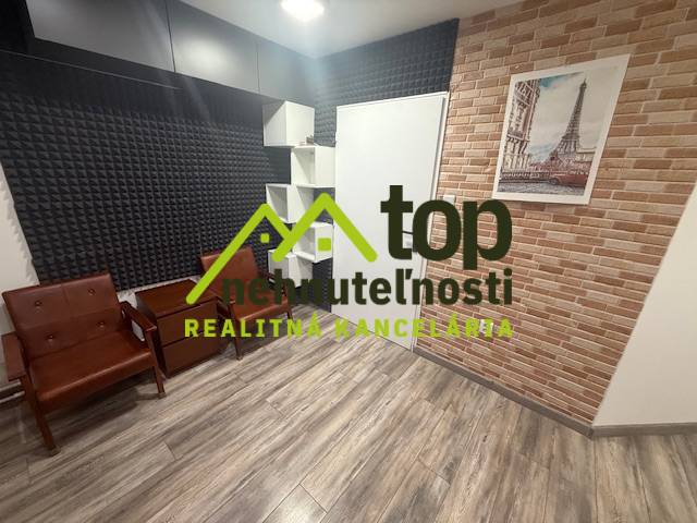 TOPOĽČANY Priestranný 1-izbový byt na prenájom 60 m2 - Izba s podlahou s dreveným dekorom a tehlovým obkladom, zariadená sedacím nábytkom.