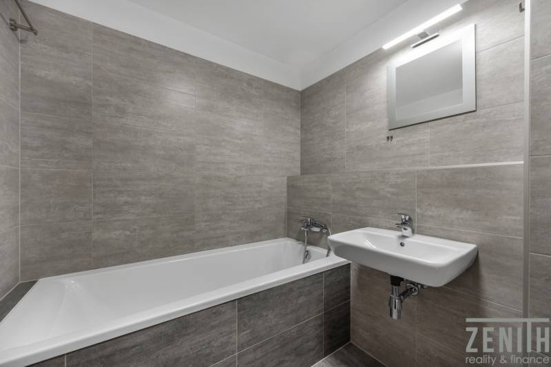 PREDAJ 2-IZBOVÉHO BYTU – NOVOSTAVBA JARABINKY, RUŽINOV - Kúpeľňa v 2-izbovom byte s vaňou, umývadlom a sivými obkladačkami.