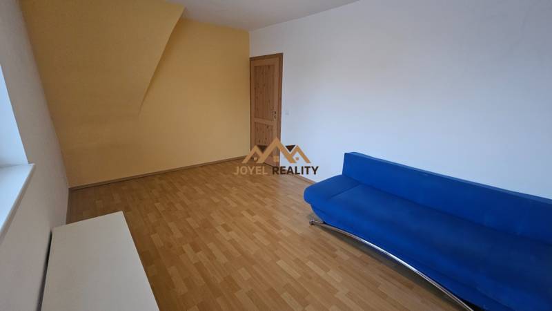 NA PRENÁJOM – PRIESTRANNÝ A SVETLÝ 3-IZBOVÝ BYT V CENTRE GALANTY - Obývacia izba v 3-izbovom byte s podlahou s dreveným dekorom a modrým gaučom.