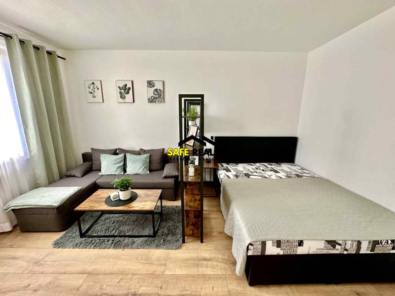 REZERVOVANÝ PREDAJ 1-izbový byt, Vlčince - okr. Žilina - Obývacia izba v 1-izbovom byte s pohovkou, posteľou a dekoráciami, podlaha s dreveným dekorom.