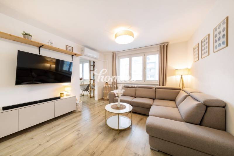 PREDAJ 2 izbový moderne zrekonštruovaný byt s klimatizáciou, CENTRUM - Obývacia izba v 2-izbovom byte s pohodlnou sedačkou a podlahou s dreveným dekorom.