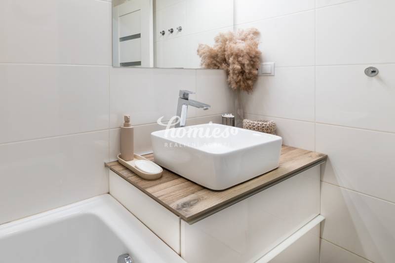 PREDAJ 2 izbový moderne zrekonštruovaný byt s klimatizáciou, CENTRUM - Kúpeľňa v 2-izbovom byte s umývadlom, podlahou s dreveným dekorom a dekoratívnym rastlinným aranžmánom.