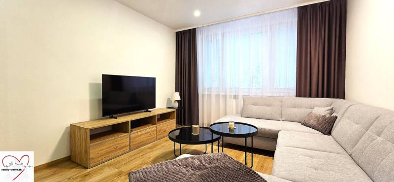 Prenájom komfortný, zariadený 3 izbový byt po úplnej rekonštrukcii - Obývacia izba v 3-izbovom byte so sedačkou, televíziou a stolíkom na podlahe s dreveným dekorom.