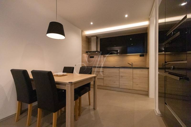 Exkluzívny 2i byt s terasou a parkovaním, Kramáre - Kuchyňa v 2-izbovom byte s dreveným dekorom, jedálenským stolom a čiernymi stoličkami.