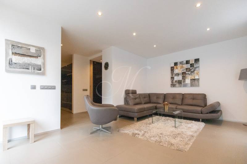 Exkluzívny 2i byt s terasou a parkovaním, Kramáre - Obývacia izba v 2-izbovom byte so sedačkou, kreslom, kobercom a obrazmi na stene.