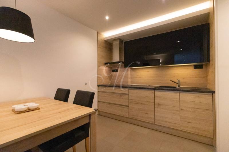 Exkluzívny 2i byt s terasou a parkovaním, Kramáre - Kuchyňa 2-izbového bytu s minimalistickým dizajnom, dreveným dekorom a jedálenským stolom.