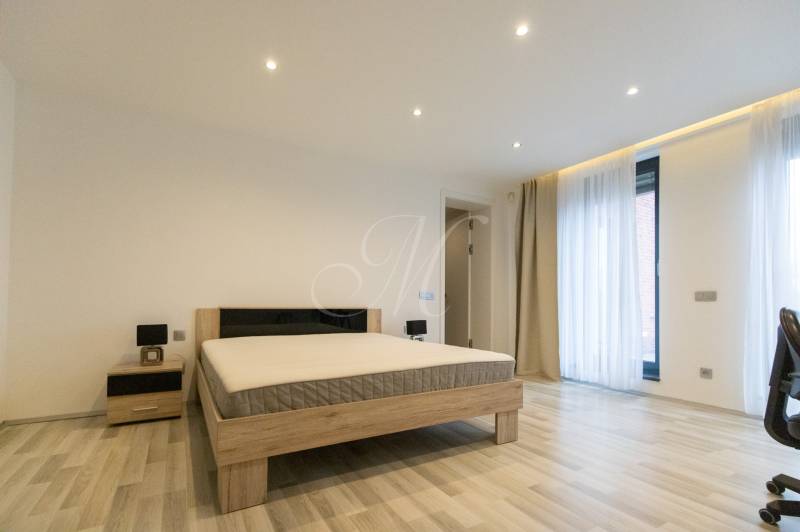 Exkluzívny 2i byt s terasou a parkovaním, Kramáre - Spálňa v 2-izbovom byte s posteľou, nočným stolíkom a podlahou s dreveným dekorom.