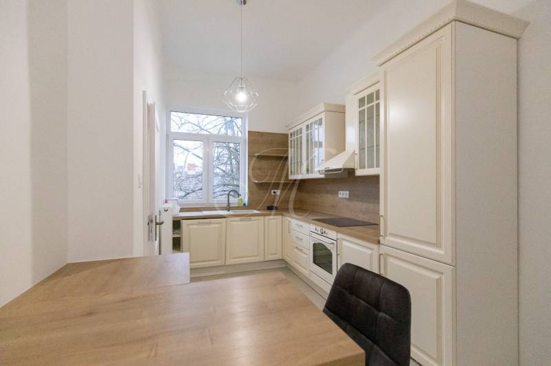 Priestranný 3i byt s vysokými stropmi, Dunajská - Kuchyňa v 3-izbovom byte s podlahou s dreveným dekorom a klasickými kuchynskými skrinkami.