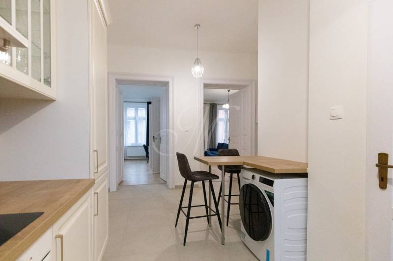 Priestranný 3i byt s vysokými stropmi, Dunajská - Chodba v 3-izbovom byte s práčkou, stoličkami a kuchynskou linkou.