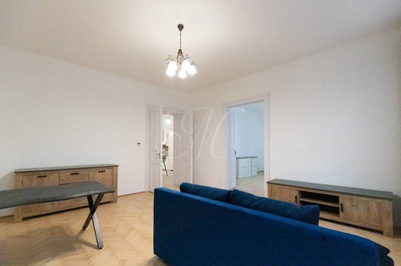 Priestranný 3i byt s vysokými stropmi, Dunajská - Obývacia izba v 3-izbovom byte s podlahou s dreveným dekorom a modrou pohovkou.