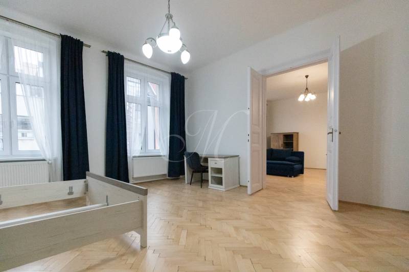 Priestranný 3i byt s vysokými stropmi, Dunajská - Interiér 3-izbového bytu s podlahou s dreveným dekorom, nábytkom a lustrom.