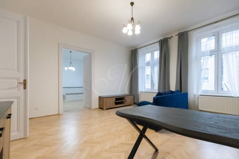 Priestranný 3i byt s vysokými stropmi, Dunajská - Obývacia izba v 3-izbovom byte s podlahou s dreveným dekorom a modrou sedačkou.