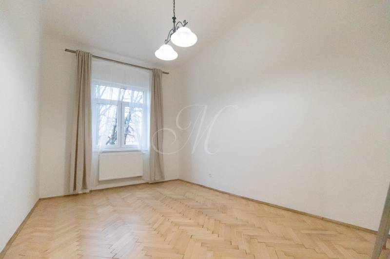 Priestranný 3i byt s vysokými stropmi, Dunajská - Izba v 3-izbovom byte s podlahou s dreveným dekorom a veľkým oknom.