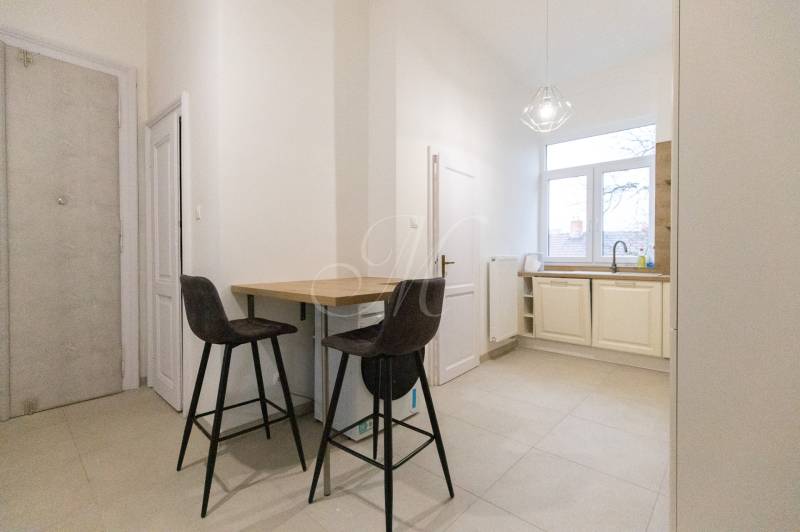 Priestranný 3i byt s vysokými stropmi, Dunajská - Kuchyňa v 3-izbovom byte s barovým pultom, dvoma stoličkami a veľkým oknom.