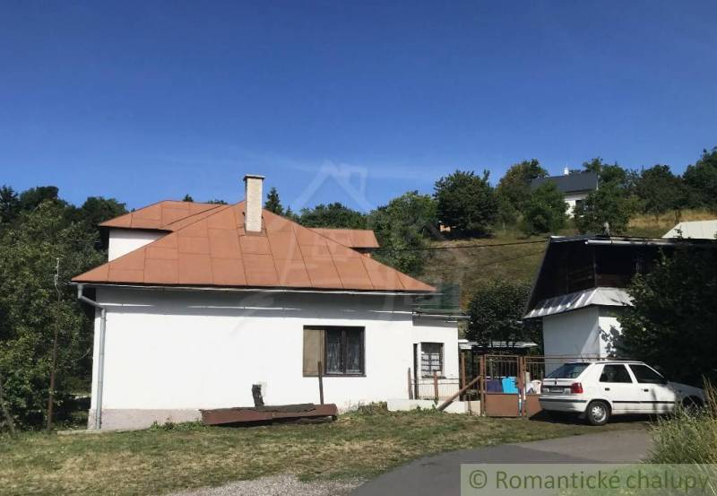 Rodinný dom v srdci Štiavnických vrchov, Štiavnické Bane. - Rodinný dom v Štiavnických Baniach s plechovou strechou, autom a stromami v pozadí.