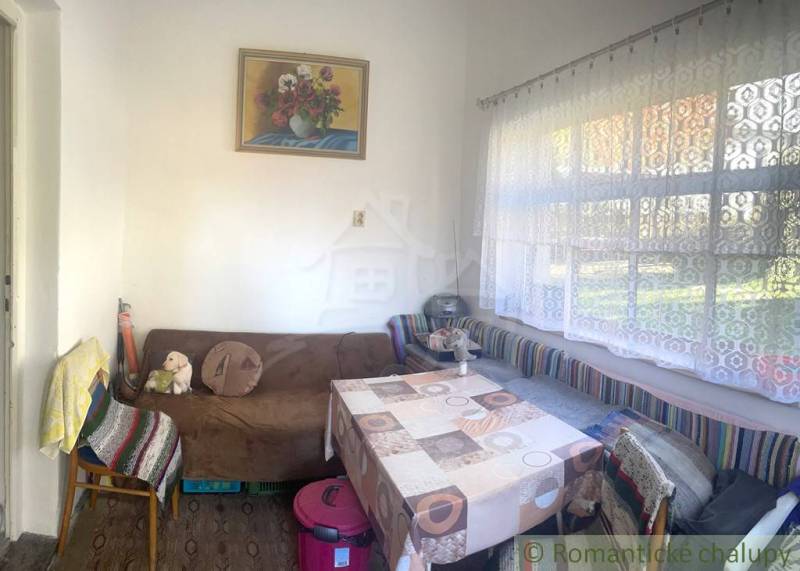 Rodinný dom v srdci Štiavnických vrchov, Štiavnické Bane. - Interiér rodinného domu s pohovkou, stolom, stoličkou a veľkým oknom s čipkovanými závesmi.