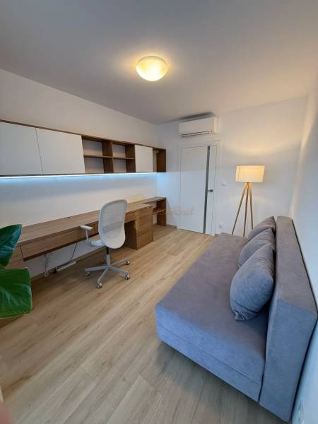 3-izb. byt, Martina Granca, Dúbravka, novostavba Pekná výhliadka - Pracovňa v 3-izbovom byte s podlahou s dreveným dekorom, sivou pohovkou a písacím stolom.