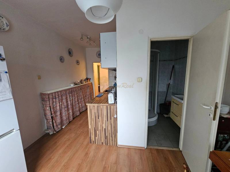 Veľký 2-izb. byt na ul. Nezábudková, Ružinov pri OC Retro - Kuchyňa v 2-izbovom byte s podlahou s dreveným dekorom a vstupom do kúpeľne.