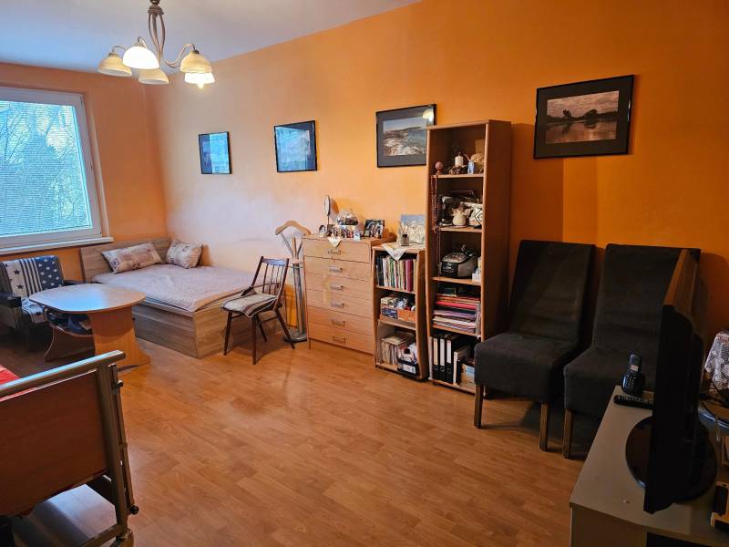 Veľký 2-izb. byt na ul. Nezábudková, Ružinov pri OC Retro - Izba s oranžovou stenou, podlahou s dreveným dekorom, posteľou a nábytkom v 2-izbovom byte.