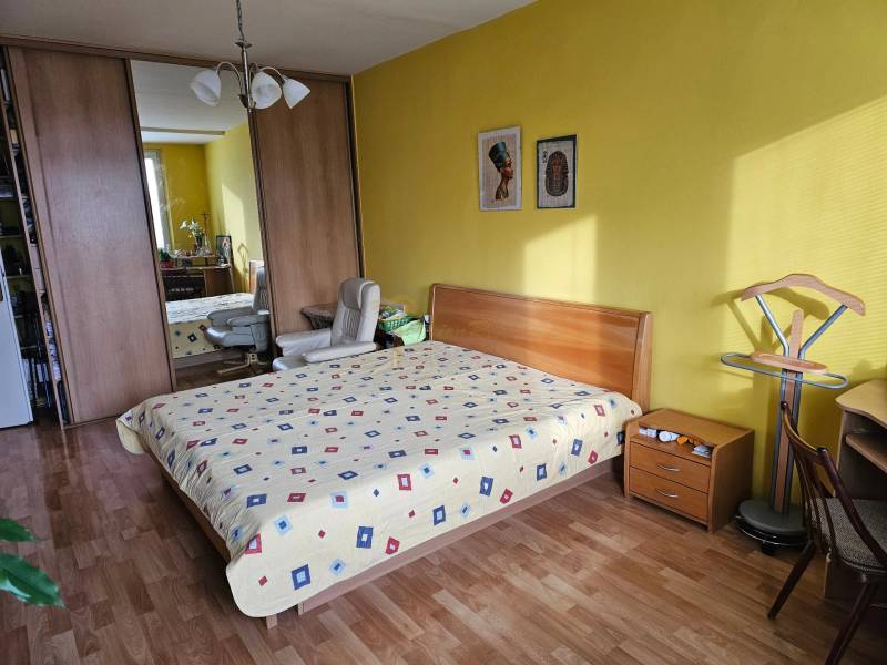 Veľký 2-izb. byt na ul. Nezábudková, Ružinov pri OC Retro - Spálňa v 2-izbovom byte s podlahou s dreveným dekorom, žltými stenami a vstavanou skriňou.
