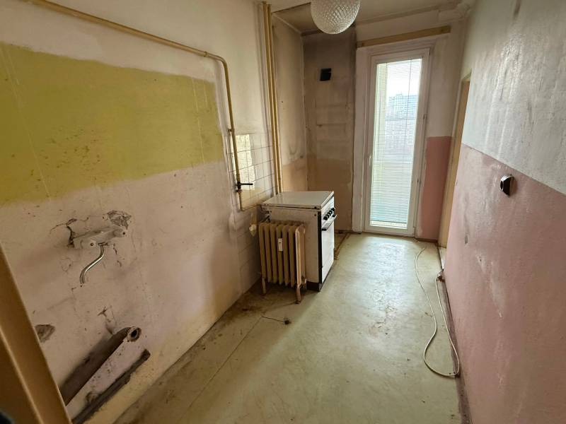 4-izb. byt, Martinčekova ul., Ružinov, 2.p./10, 2 x lodžia - Stará kuchyňa v 4-izbovom byte s opotrebovanými stenami a sporákom pri okne.