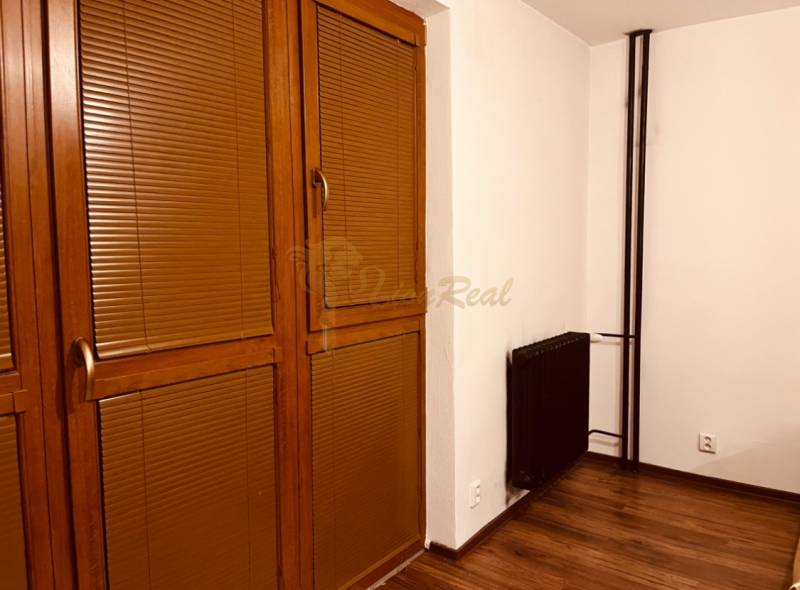 Garzónka M. Schneidra Trnavského, Dúbravka, veľká lodžia - Garsónka s hnedými žalúziami, dverami a podlahou s dreveným dekorom, radiátor v rohu.