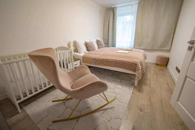 2,5 izb. byt, ul. Jelenia, Staré Mesto,tehlový dom, po rekonštrukcii - Spálňa s posteľou, drevenou podlahou, detskou postieľkou a hojdacím kreslom, na ulici Jelenia.