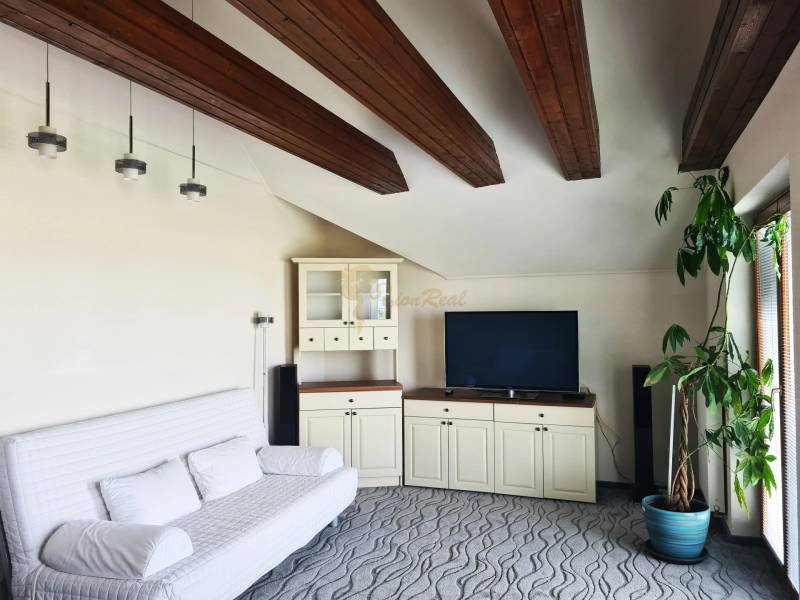 5-izb. dvojpodlažný rodinný dom, Rovinka - Obývačka v rodinnom dome so stropnými trámami, pohovkou, televíziou a veľkou rastlinou.