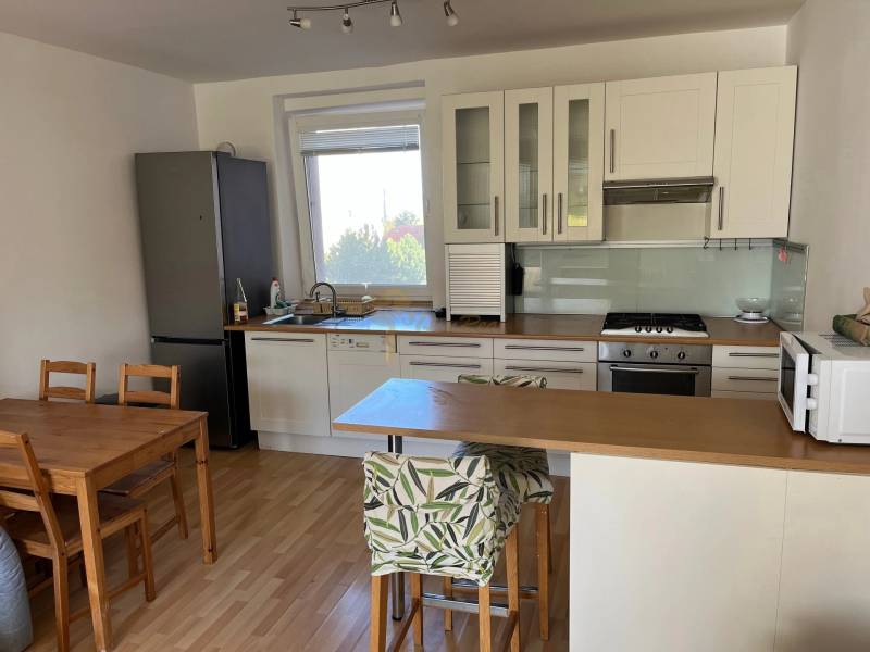 3-izb. byt, Palkovičova ul., Ružinov, lodžia, 4.p./12 - Kuchyňa v 3-izbovom byte s podlahou s dreveným dekorom, jedálenským stolom a barovým pultom.