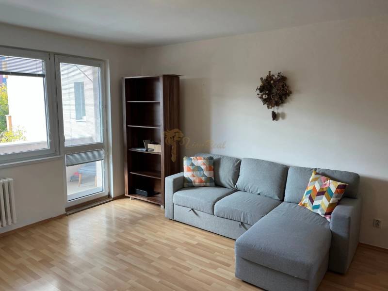 3-izb. byt, Palkovičova ul., Ružinov, lodžia, 4.p./12 - Obývacia izba v 3-izbovom byte so sedačkou, policou a podlahou s dreveným dekorom.