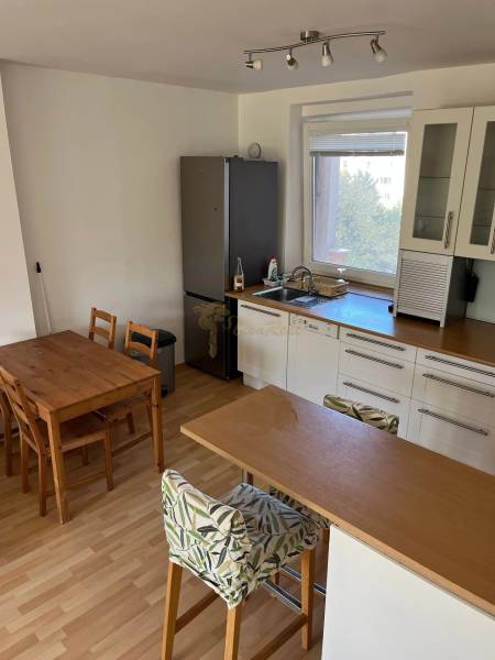 3-izb. byt, Palkovičova ul., Ružinov, lodžia, 4.p./12 - Kuchyňa v 3-izbovom byte s barovým pultom, jedálenským stolom a podlahou s dreveným dekorom.