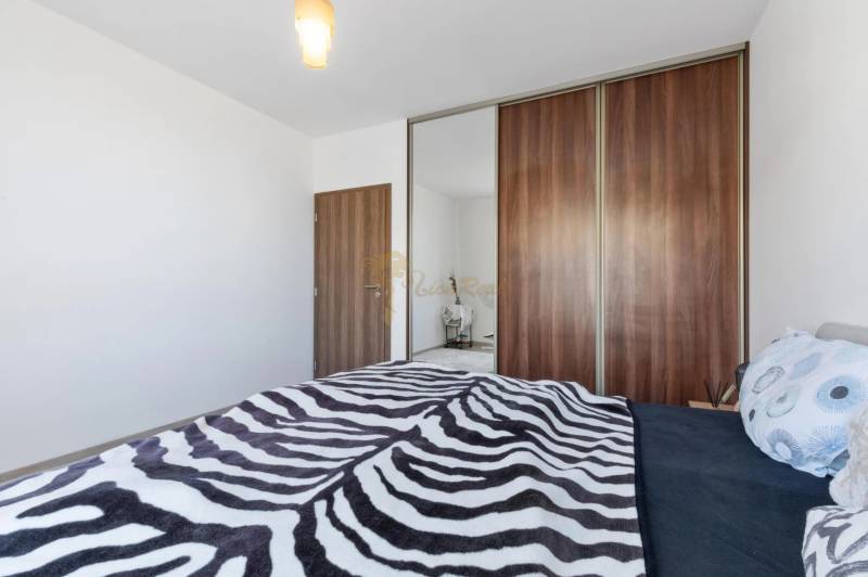 Novostavba 3-izb. bytu s parkovacím státím, ul.Hany Ponickej, Lamač - Spálňa s posteľou a veľkou skriňou v 3-izbovom byte, vešiak s ozdobnými vankúšmi.