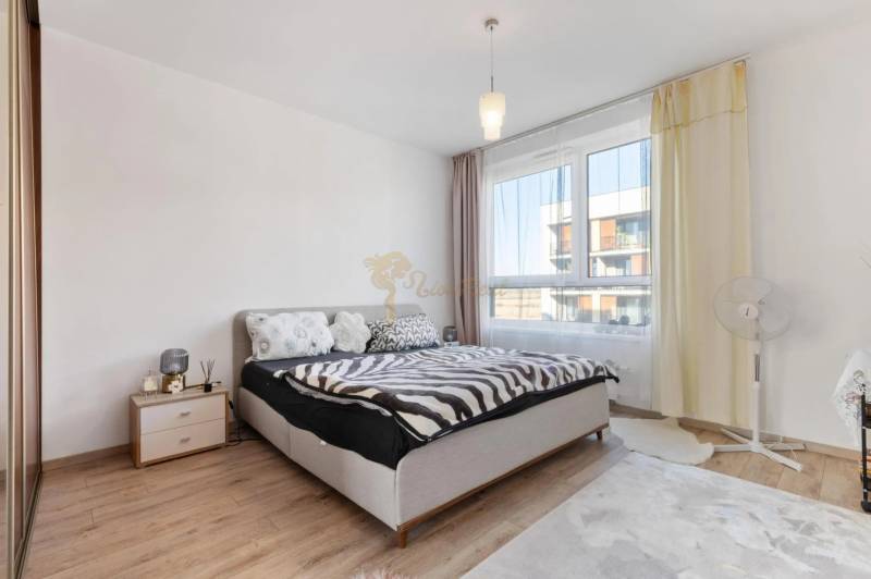 Novostavba 3-izb. bytu s parkovacím státím, ul.Hany Ponickej, Lamač - Svetlá spálňa v 3-izbovom byte s posteľou, nočným stolíkom a podlahou s dreveným dekorom.