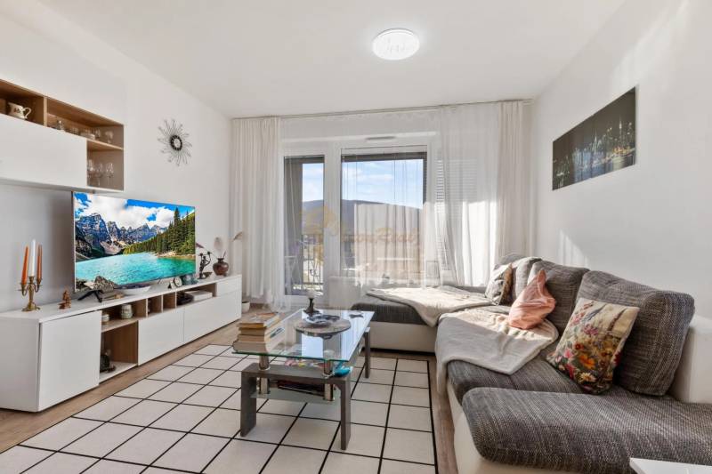 Novostavba 3-izb. bytu s parkovacím státím, ul.Hany Ponickej, Lamač - Obývačka v 3-izbovom byte s pohodlným sedením a stolíkom, podlaha s dreveným dekorom.