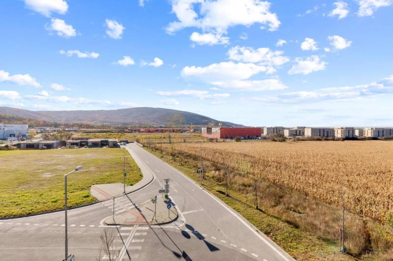 Novostavba 3-izb. bytu s parkovacím státím, ul.Hany Ponickej, Lamač - Cesta a polia vo štvrti Bratislava - Lamač, Hany Ponickej, obklopené budovami.