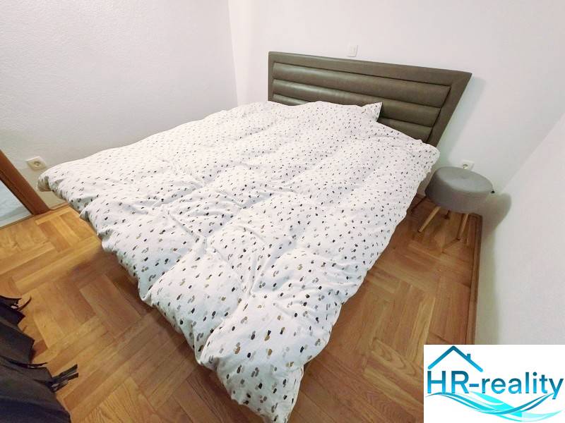 Chorvátsko, Makarska - zariadený apartmán s výhľadom na more - Rekreačný apartmán s posteľou, dreveným dekorom podlahy a malým nočným stolíkom.