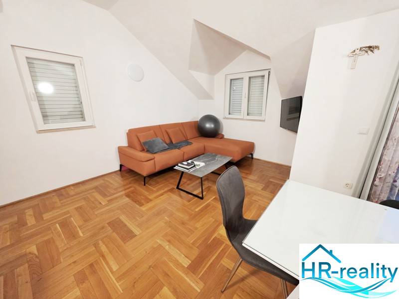 Chorvátsko, Makarska - zariadený apartmán s výhľadom na more - Rekreačný apartmán s oranžovou sedačkou a podlahou s dreveným dekorom.