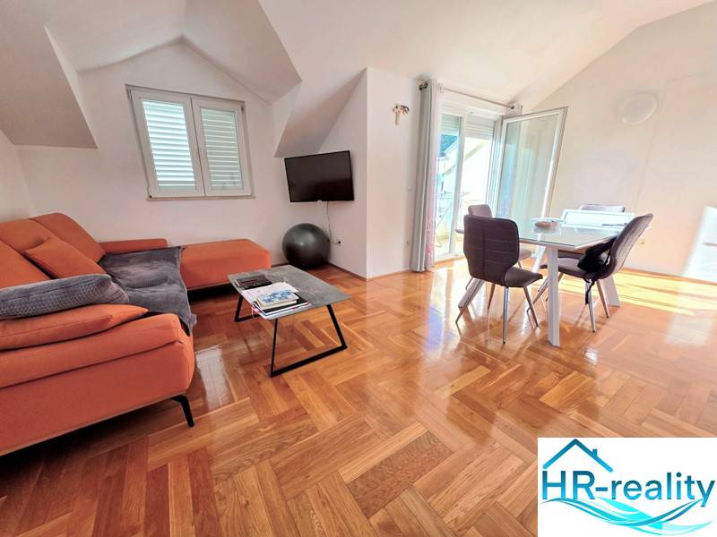 Chorvátsko, Makarska - zariadený apartmán s výhľadom na more - Rekreačný apartmán s oranžovou pohovkou, jedálenským stolom a podlahou s dreveným dekorom.