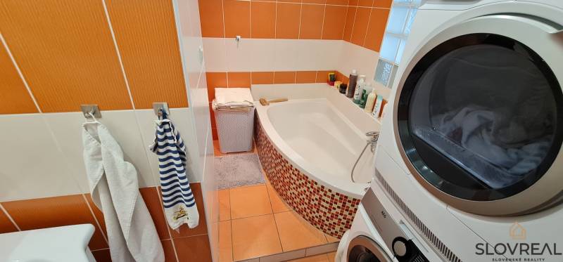 Predaj 2i byt v meste Kremnica, 64m2 - Kúpeľňa s vaňou a práčkou v 2-izbovom byte s oranžovými obkladačkami.